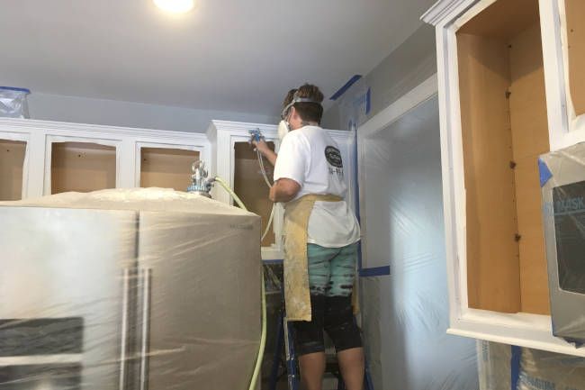 Painter spraying kitchen cabinet boxes with the room masked in plastic