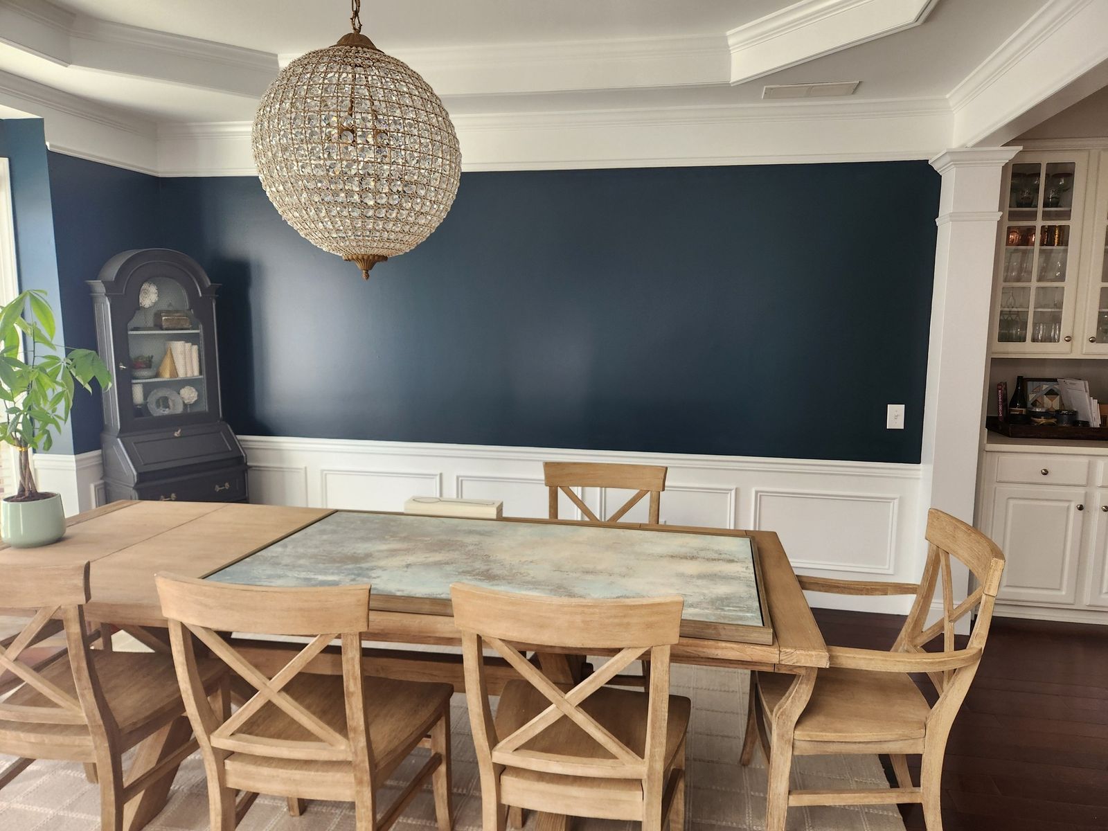 Dining room painted navy above white wainscoting, with a round chandelier
