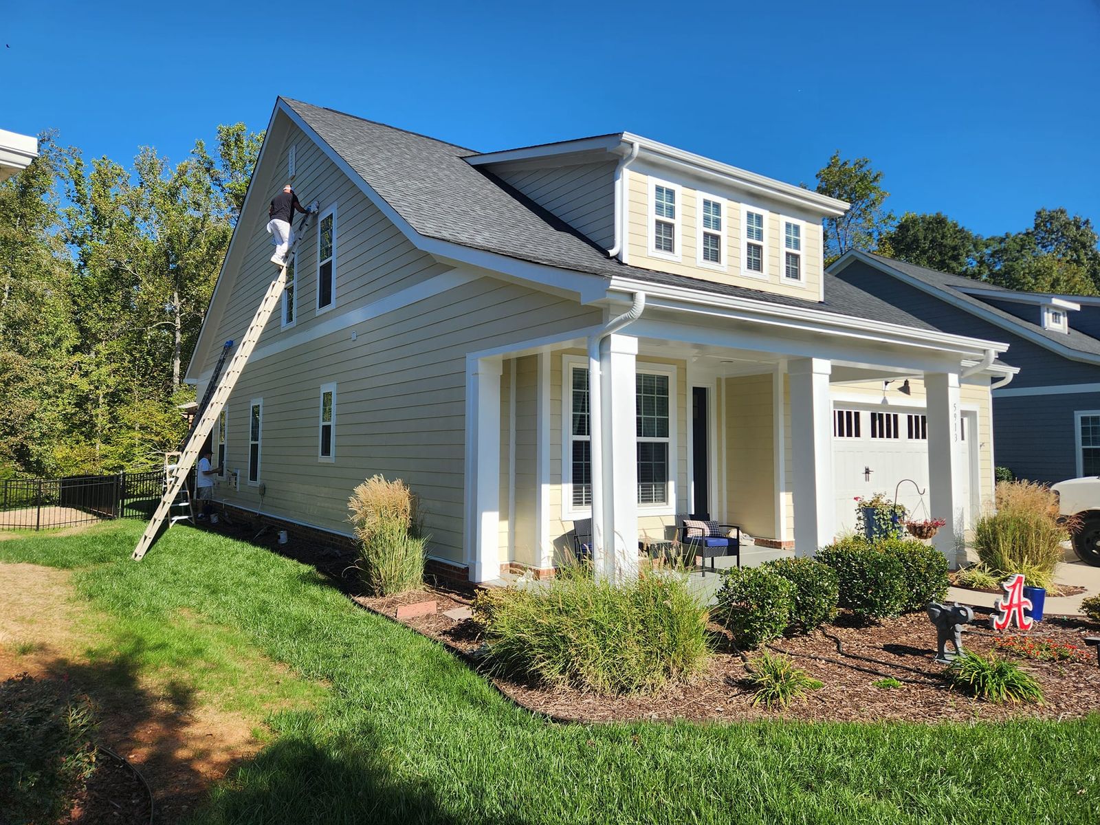 Two-story home exterior with a painter working from a ladder