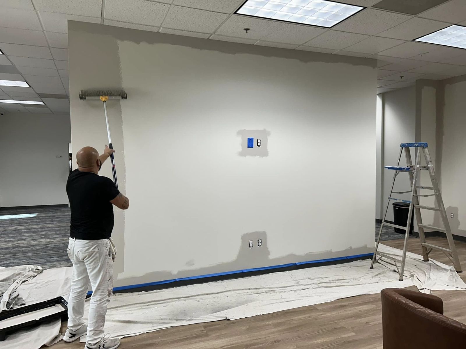 Painter rolling a wall in an office with the floor covered